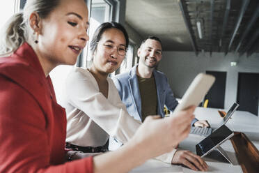 Geschäftsfrau, die ihr Smartphone bei einer Besprechung im Büro benutzt - UUF28385