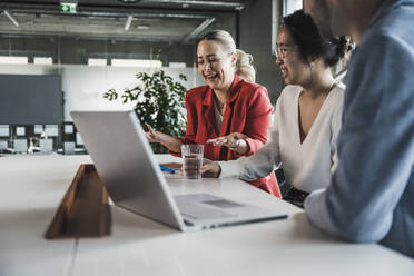 Businesswoman laughing with colleagues sitting at desk in office - UUF28390