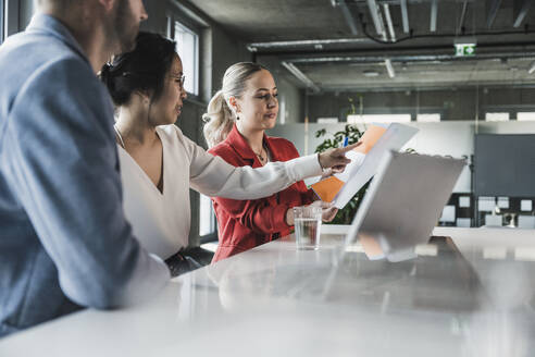 Businesswoman pointing at folder in discussion with colleagues at office - UUF28391