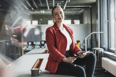 Junge Geschäftsfrau mit Tablet-PC an einem Schreibtisch im Büro sitzend - UUF28400