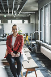 Smiling businesswoman with tablet PC sitting on desk in office - UUF28402