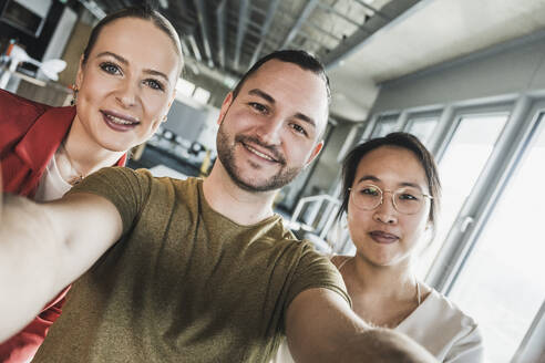 Smiling businessman taking selfie with colleagues at office - UUF28405