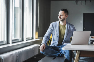 Kontemplativer Geschäftsmann mit Laptop auf einer Bank im Büro sitzend - UUF28409