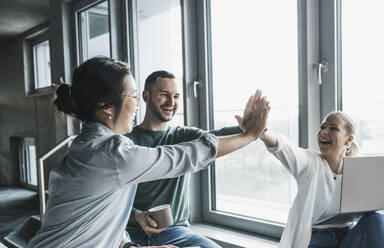 Happy business colleagues giving high-five to each other at office - UUF28425