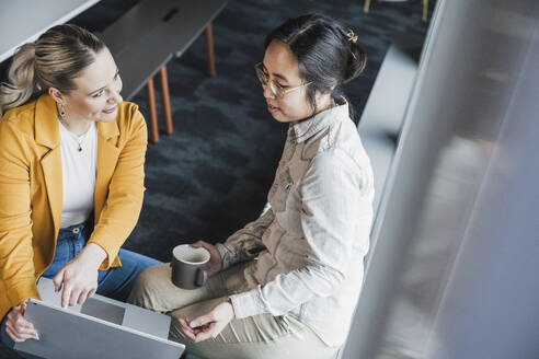 Geschäftsfrauen, die im Büro sitzen und miteinander diskutieren - UUF28458