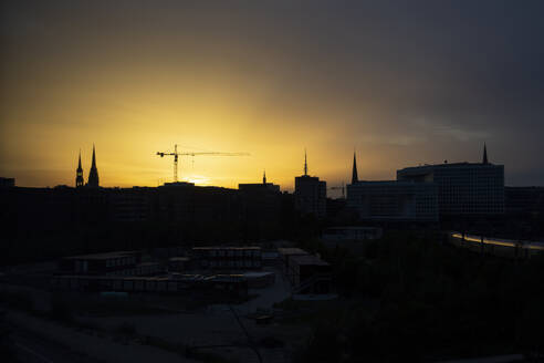 Deutschland, Hamburg, Silhouetten von Stadttürmen und Baukran bei Sonnenuntergang - ASCF01730