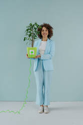Glückliche Frau, die mit einem an einer Topfpflanze befestigten Elektrostecker steht - YTF00578