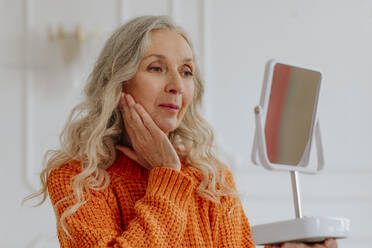 Ältere Frau mit grauen Haaren schaut in den Spiegel zu Hause - MDOF00842