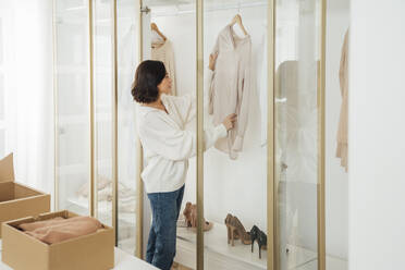 Young woman checking clothes hanging in closet at home - VPIF07879