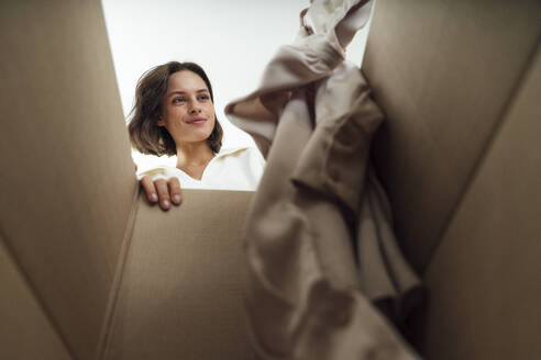 Lächelnde Frau packt Kleidung in einen Karton - VPIF07915