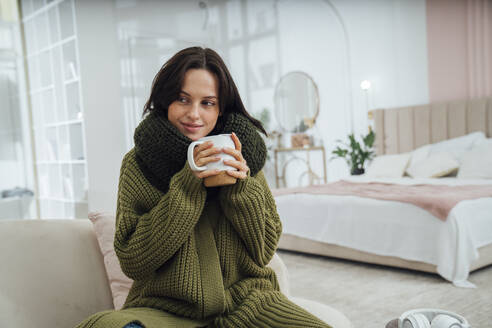 Lächelnde junge Frau mit Kaffeetasse im Schlafzimmer zu Hause sitzend - VPIF07941