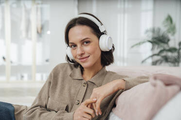 Lächelnde Frau mit drahtlosen Kopfhörern im Schlafzimmer sitzend - VPIF07956