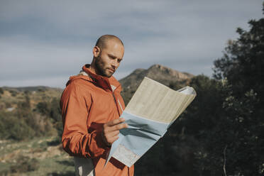 Smiling man reading map standing in nature - DMGF01077