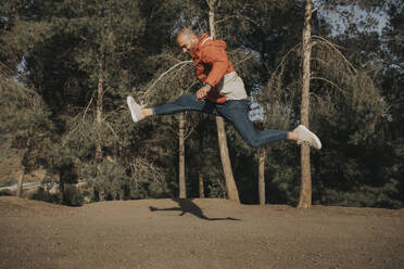 Man jumping in front of trees on sunny day - DMGF01081