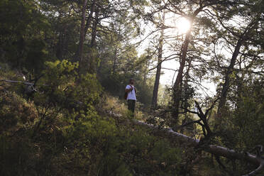 Hiker standing on tree log in forest - SYEF00249