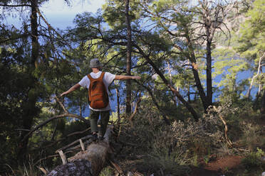 Hiker with arms outstretched balancing on tree trunk - SYEF00252