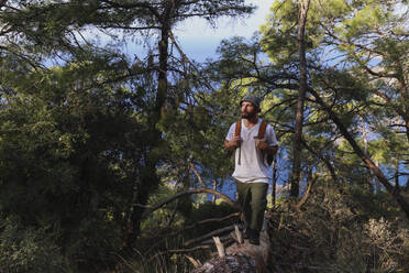 Wanderer auf Baumstamm genießt Sonnenlicht auf Gesicht im Wald - SYEF00253
