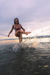Happy young woman splashing water at beach - PNAF05015