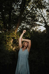 Junge Frau mit erhobenem Arm vor einem Baum stehend - GMLF01311