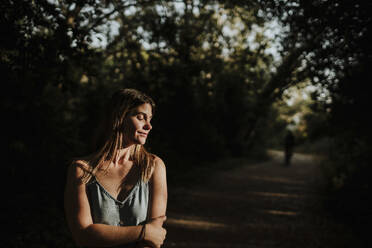 Lächelnde junge Frau mit geschlossenen Augen im Wald stehend - GMLF01314