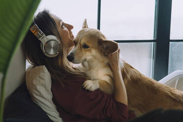 Lächelnde Frau, die mit ihrem Hund zu Hause über Kopfhörer Musik hört - IEF00314