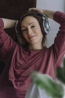 Lächelnde Frau mit drahtlosen Kopfhörern zu Hause - IEF00316