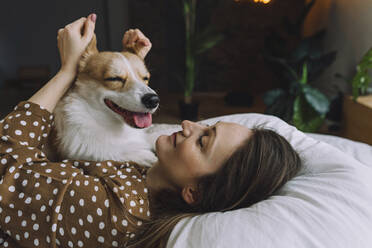 Lächelnde Frau spielt mit Hundeohren auf dem Bett liegend zu Hause - IEF00328