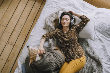 Sorglose Frau, die zu Hause auf dem Bett liegend über Kopfhörer Musik hört - IEF00330