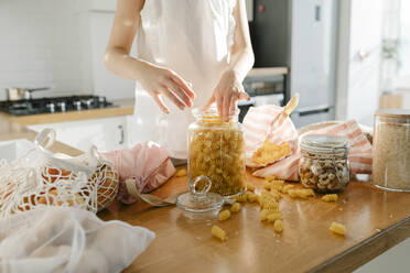 Girl with pasta in glass jar on kitchen island at home - SSYF00136