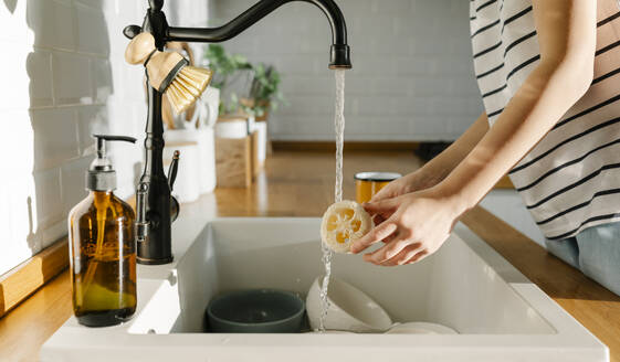 Girl washing loofah in sink at home - SSYF00138