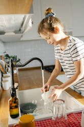 Mädchen wäscht Geschirr im Waschbecken zu Hause - SSYF00141