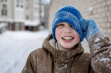 Happy boy wearing blue knit hat in snow - ANAF01074