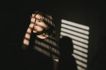 Blinds shadow on boy covering eye with hand - ANAF01075