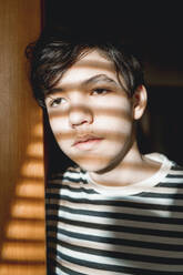 Nachdenklicher Jugendlicher mit Sonnenlicht im Gesicht an der Tür stehend - ANAF01081