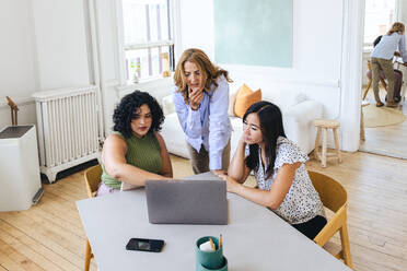 Female colleagues brainstorming over laptop at table in office - CAVF96615