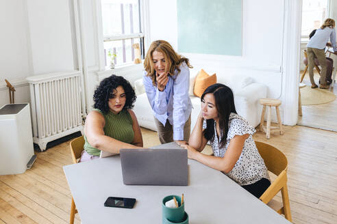 Weibliche Kollegen beim Brainstorming mit Laptop am Tisch im Büro - CAVF96615