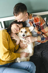 Young couple embracing and playing with Pembroke Welsh Corgi at home - VBUF00278