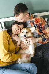 Couple embracing and playing with Pembroke Welsh Corgi sitting at home - VBUF00279