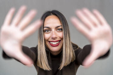 Happy woman making finger frame against gray background - DLTSF03580