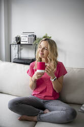 Thoughtful mature woman sitting with coffee cup at home - HMEF01526