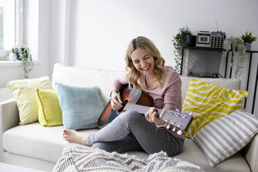Glückliche reife Frau spielt Gitarre auf dem Sofa zu Hause - HMEF01531