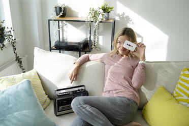 Lächelnde Frau mit Kassette und Radio auf dem Sofa zu Hause - HMEF01539