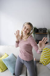 Smiling mature woman wearing wireless headphones dancing at home - HMEF01543