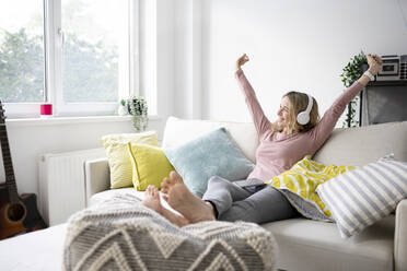 Happy mature woman with arms raised sitting on sofa at home - HMEF01545