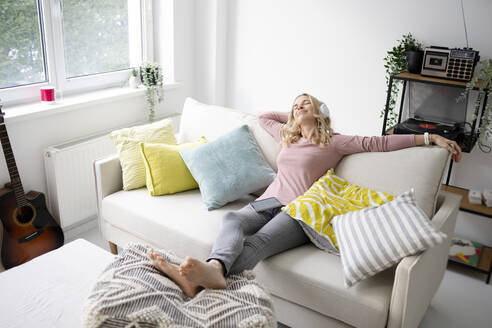 Lächelnde reife Frau mit geschlossenen Augen sitzt zu Hause auf dem Sofa - HMEF01546