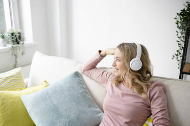 Thoughtful mature woman wearing wireless headphones sitting at home - HMEF01547