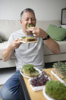 Mature man with eyes closed eating sprouts at home - HMEF01555