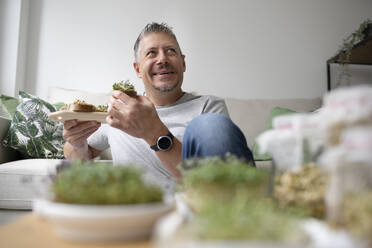 Thoughtful mature man eating sprouts at home - HMEF01556