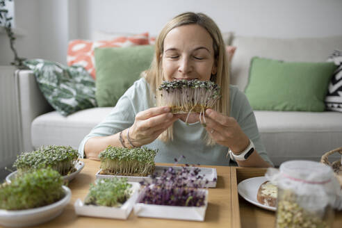 Woman smelling seedlings at home - HMEF01560