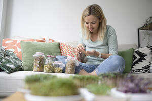 Frau mit verschiedenen Bohnensprossengläsern auf dem Sofa zu Hause - HMEF01564